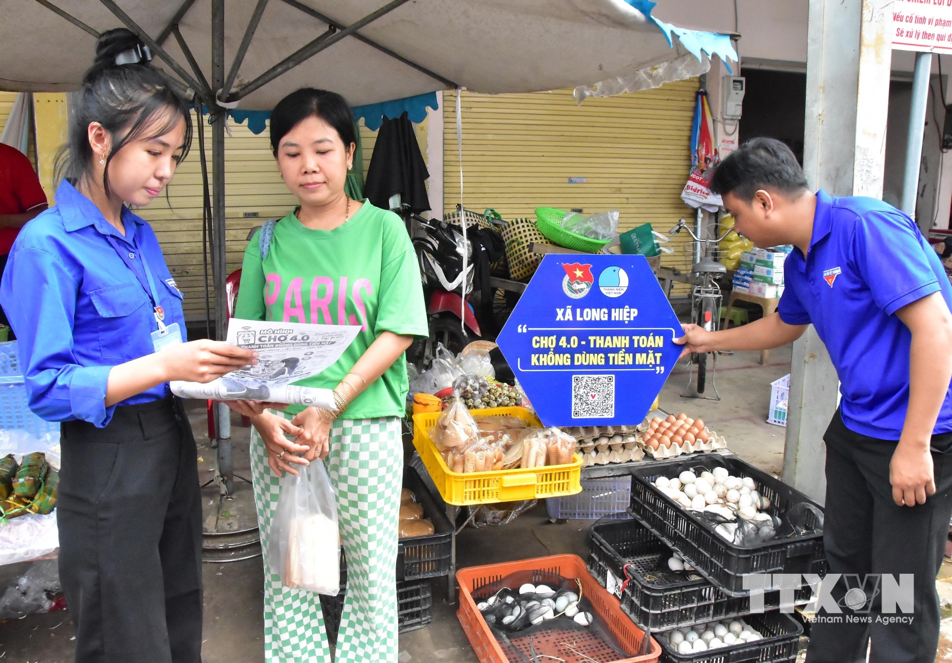 Đoàn viên hướng dẫn tiểu thương và người dân ở chợ Long Hiệp quét QR thanh toán không dùng tiền mặt. (Ảnh: Thanh Hòa/TTXVN)